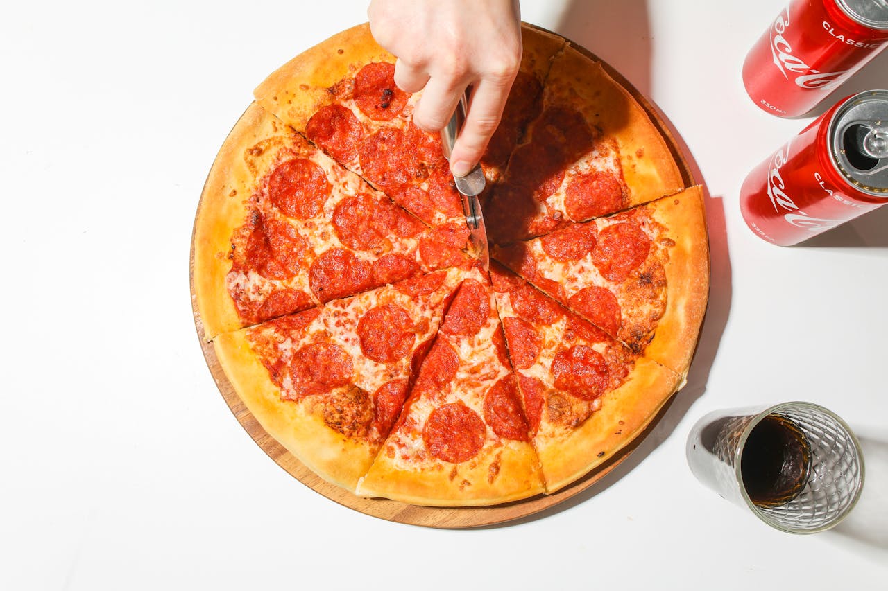 Mastering the First Impression: Your intriguing post title goes here A delicious pepperoni pizza being sliced with classic soda cans for a tasty meal.